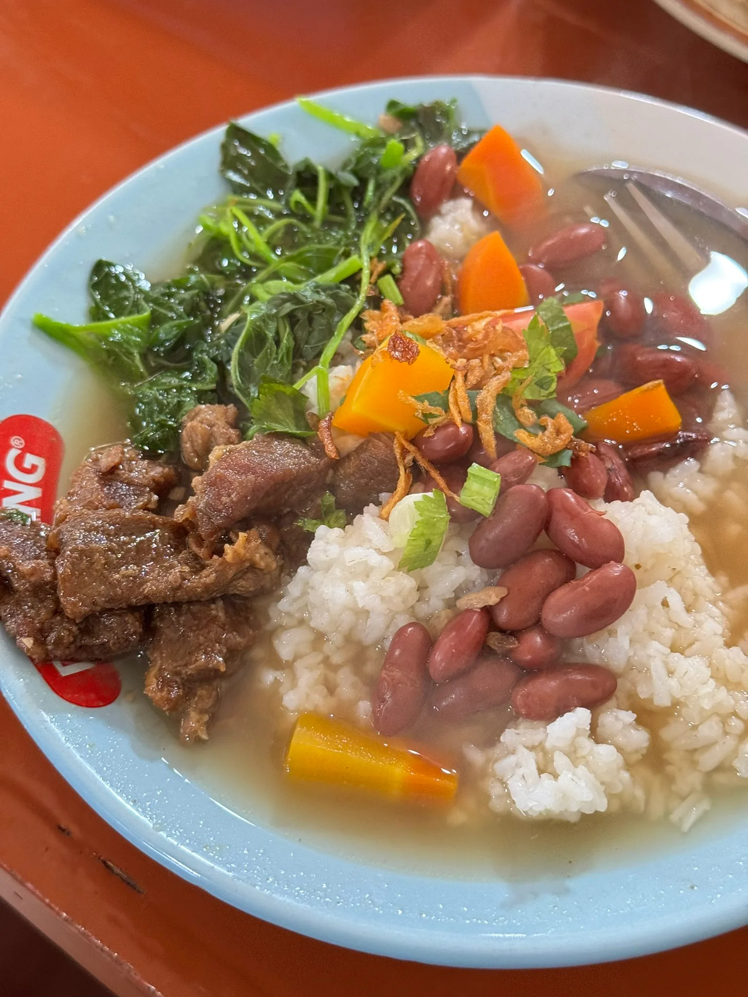 A close-up of Sop Senerek with red beans and vegetables in a clear broth
