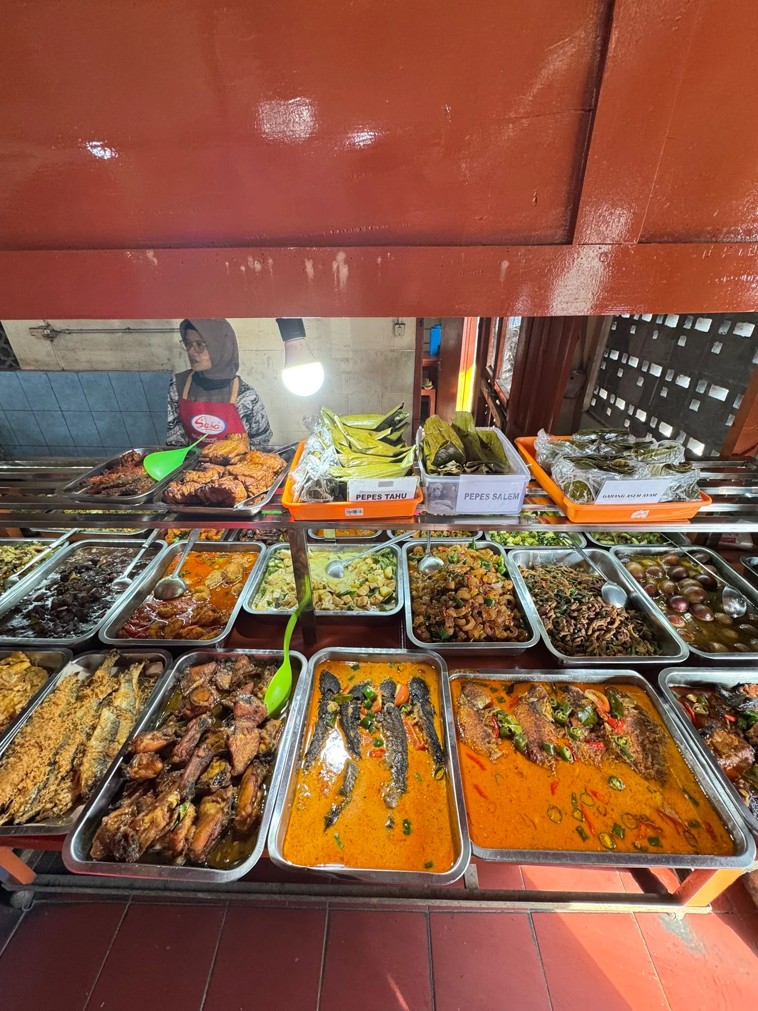 Plates of cooked dishes arranged in trays waiting for customers at a warung